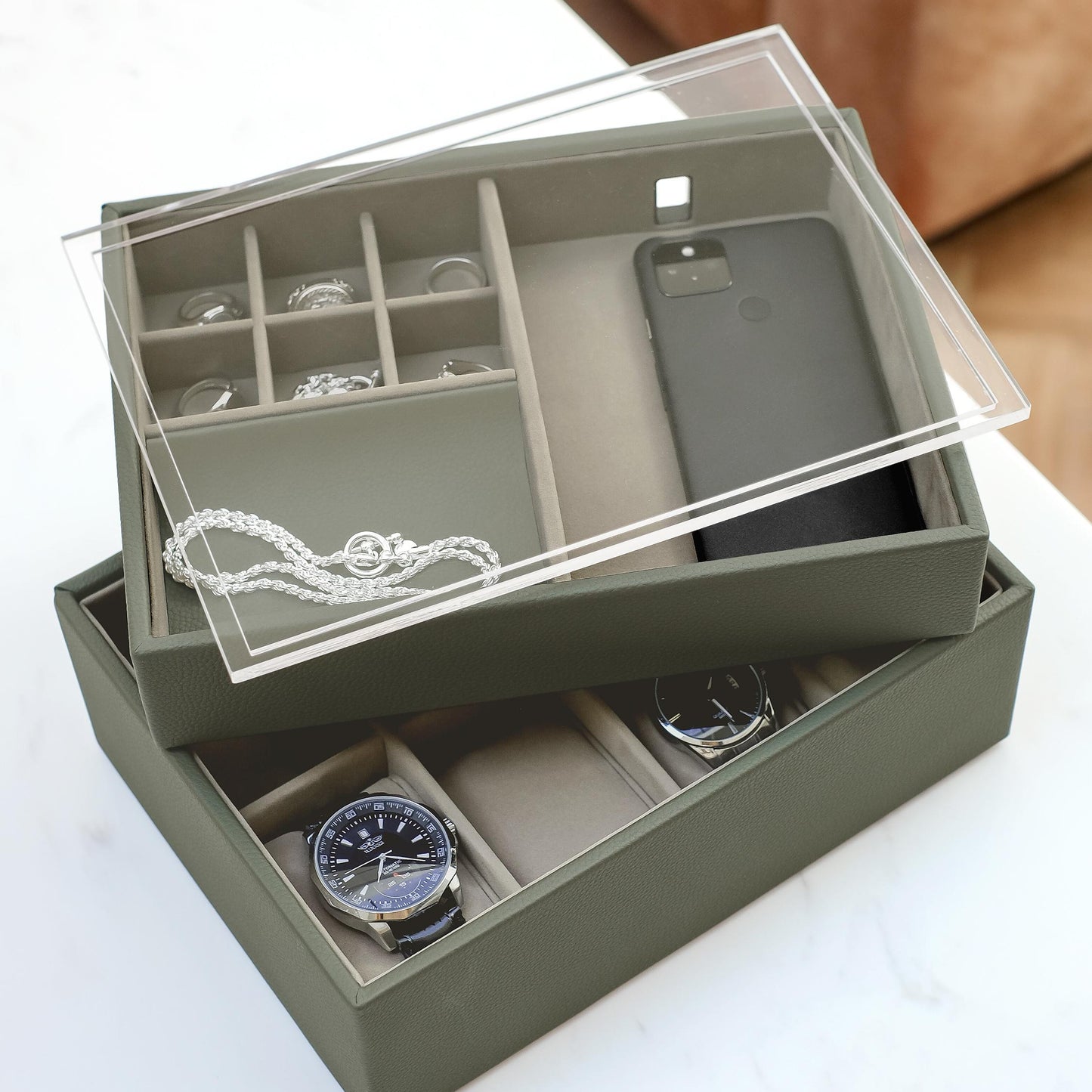 Green jewelry box with clear top compartment containing a phone, watch, and other items on a white surface.
